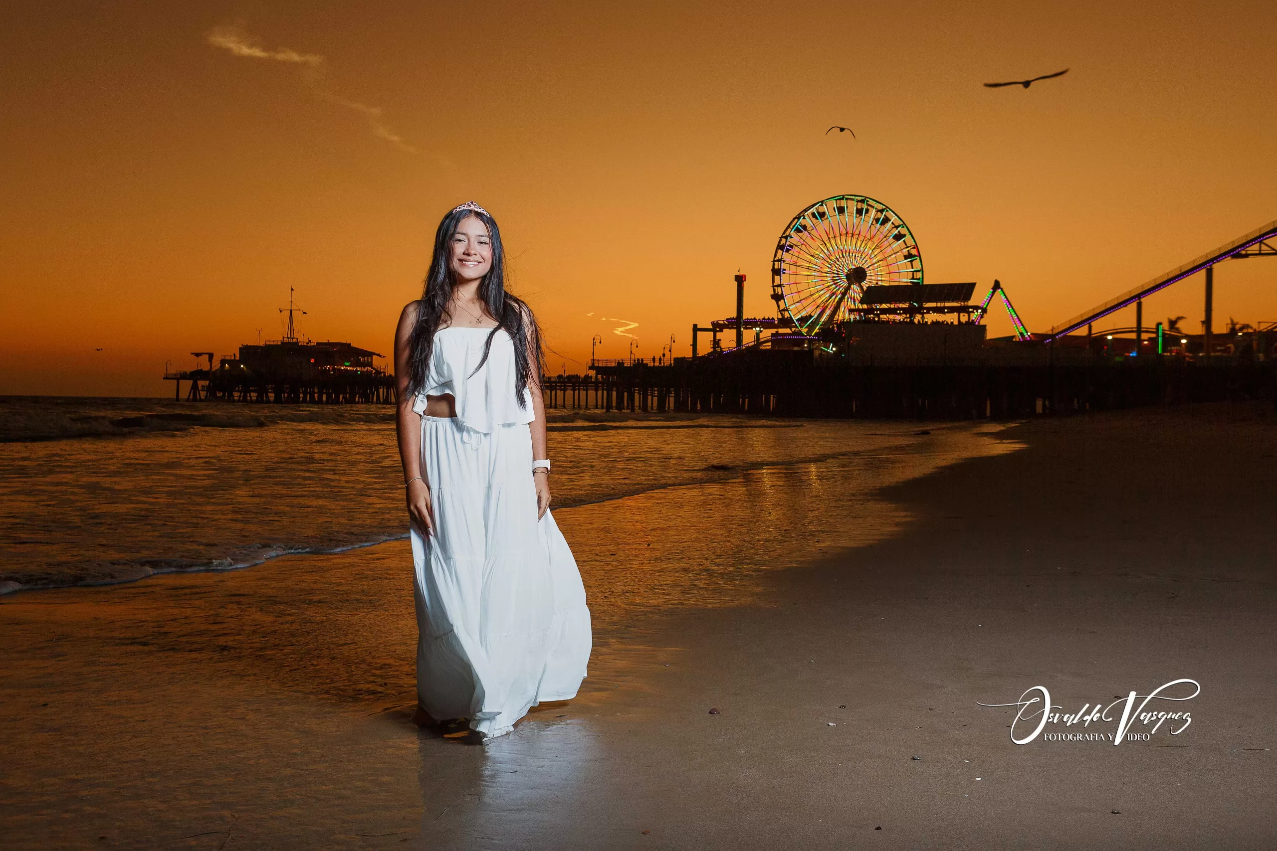 fotografia y video para quinceanera sweet sixteen 2 En la playa de Santa Mónica, Los Ángeles, California, una joven camina sobre la arena dorada con el reflejo del atardecer en el mar, mientras la rueda de la fortuna ilumina el horizonte como un sueño hecho realidad.